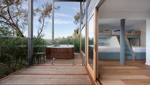 Una terraza moderna al aire libre con un jacuzzi, un dormitorio con literas y paredes de vidrio, y vistas a la vegetación circundante.