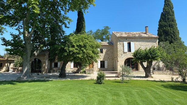 A stone building with a tiled roof, surrounded by well-maintained grass and trees. - Le Mas in the shade of the plane trees (Cavaillon)