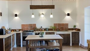 A spacious kitchen with wooden beams, a central island with glassware, and a rustic aesthetic. - Le Mas in the shade of the plane trees (Cavaillon)