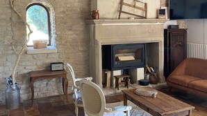 A rustic living room with exposed wooden beams, a stone wall, a fireplace, a television, and a comfortable seating area. - Le Mas in the shade of the plane trees (Cavaillon)