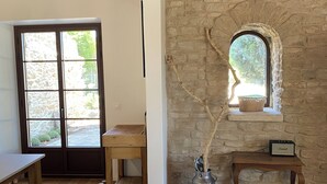 A rustic room with stone walls, a wooden table, a bench, and a window with a view of greenery. - Le Mas in the shade of the plane trees (Cavaillon)
