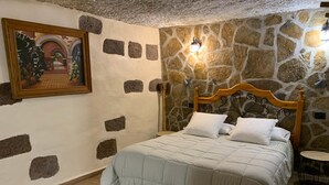 Un dormitorio con pared de piedra, una cama con ropa de cama blanca, un cuadro en la pared y una alfombra redonda.