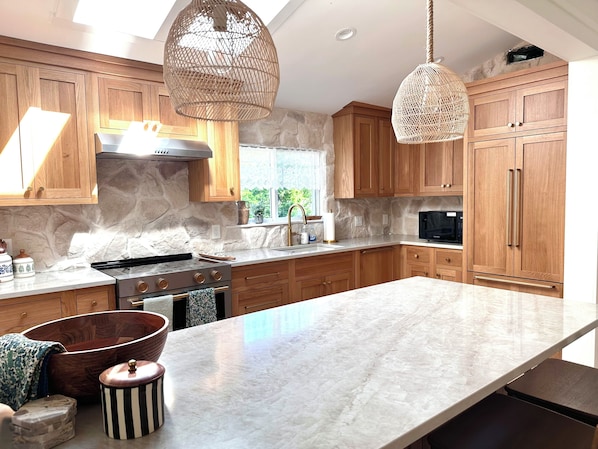 A modern kitchen with wooden cabinets, a large island, a stove, and hanging wicker light fixtures.