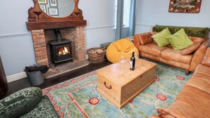 A cozy living room with a brick fireplace, a wooden coffee table, a leather sofa, and a patterned rug. - Rosemary Cottage (Leyburn)