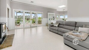 A spacious living room with a grey sofa, a fireplace, and a view of a garden through large glass doors.