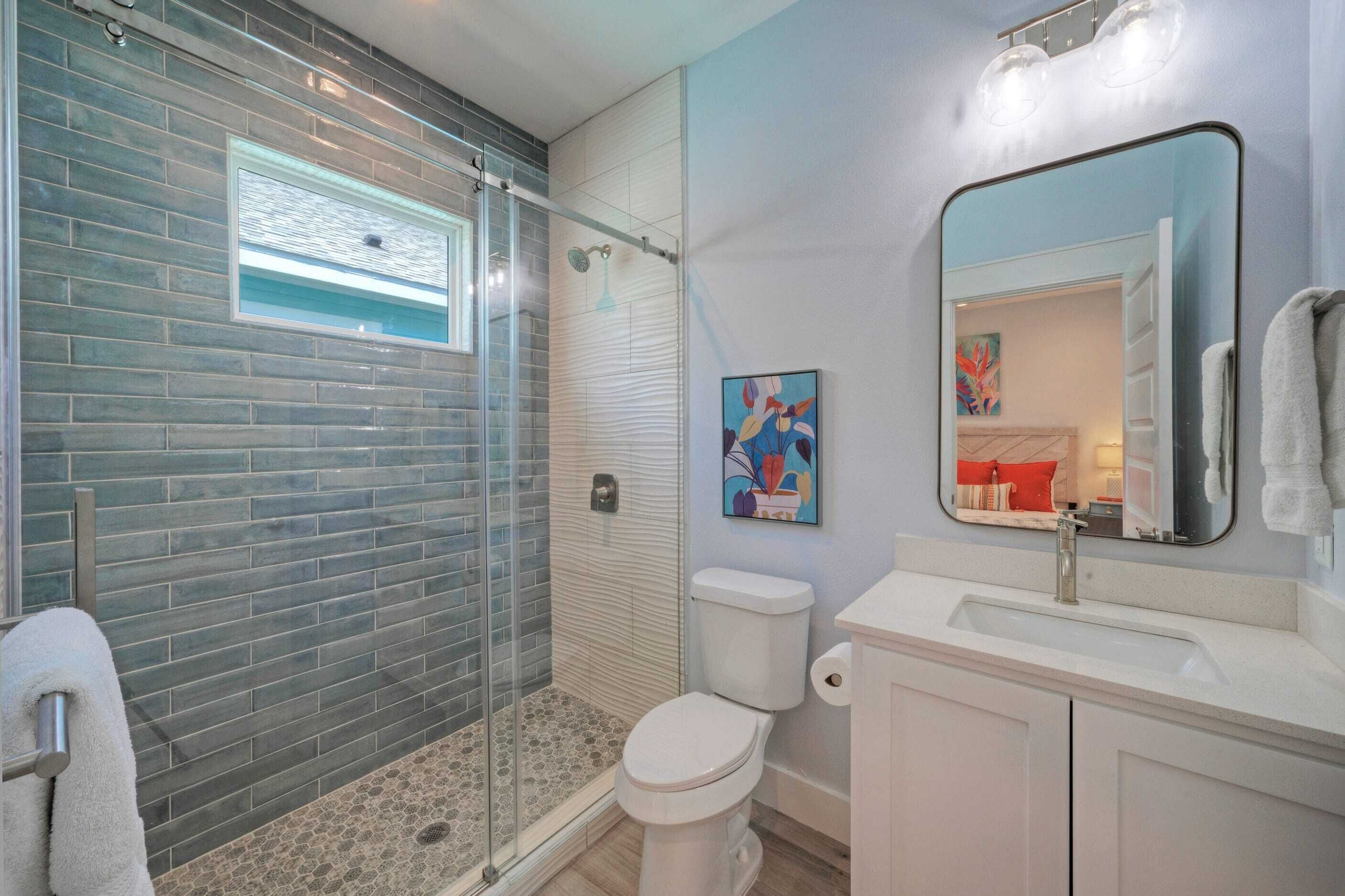 A modern bathroom with a glass shower enclosure, a white toilet, and a sink with a mirror.