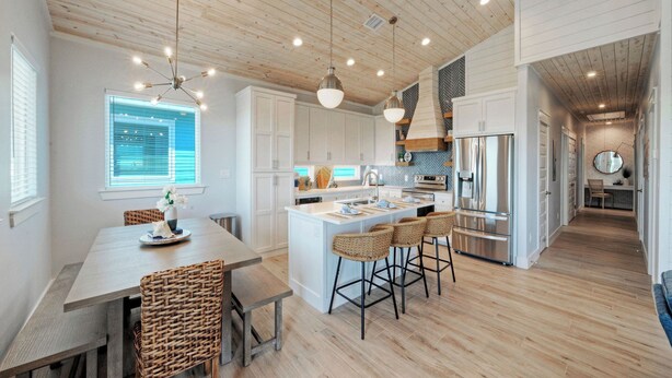 Una cocina moderna con armarios blancos, una isla central con taburetes altos y un refrigerador de acero inoxidable.
