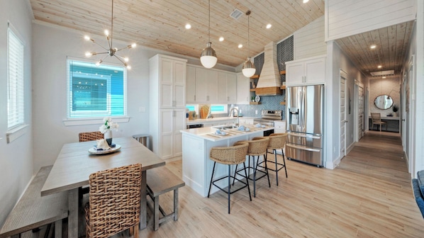 A modern kitchen with white cabinetry, a central island with bar stools, and a stainless steel refrigerator.