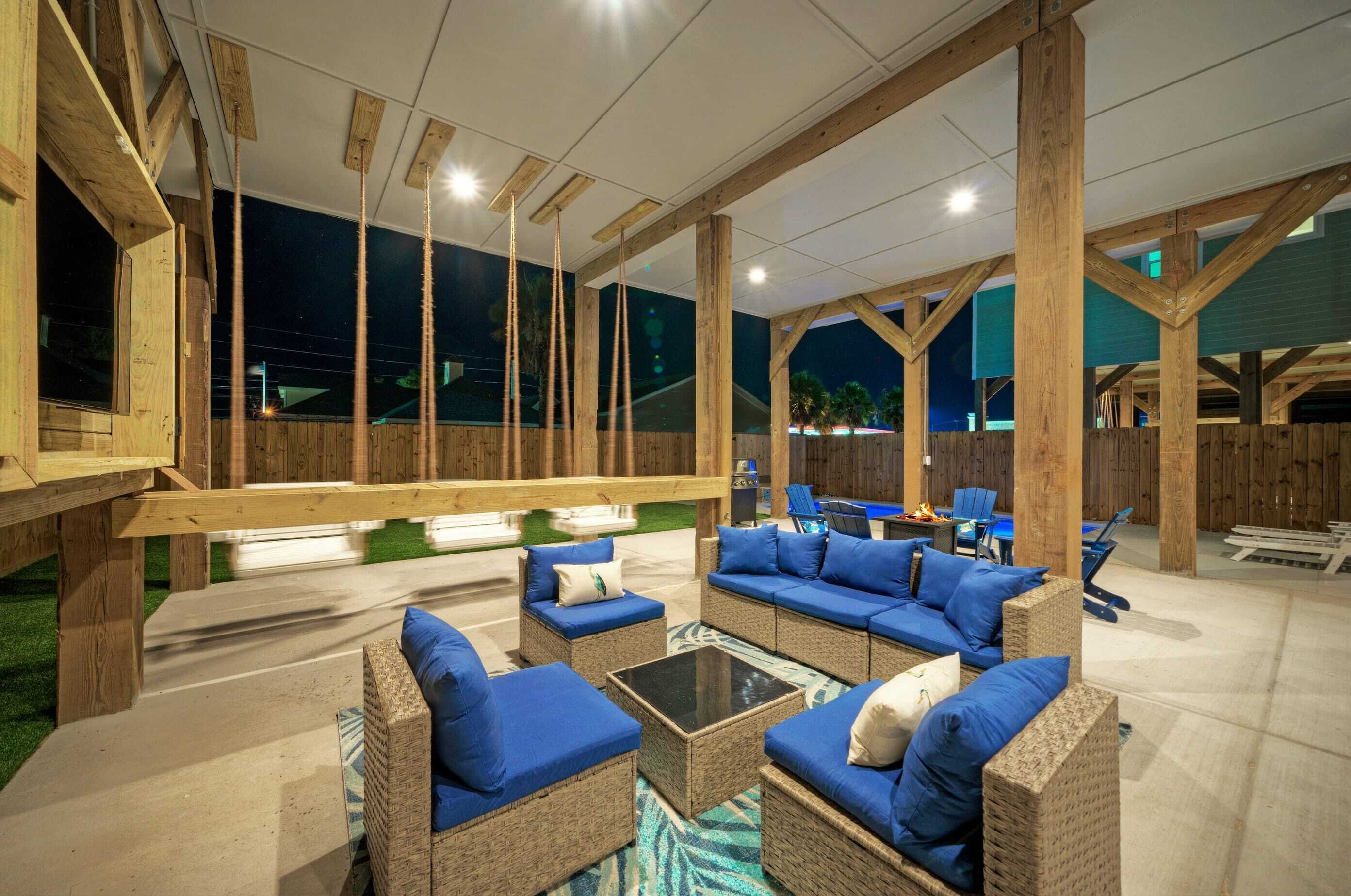 Un espace extérieur aménagé en terrasse, avec des meubles en osier, des coussins bleus et une table basse avec un plateau en verre.