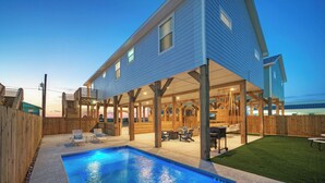 Una casa de dos pisos con un porche cubierto, una piscina y un patio trasero cercado.