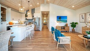 A spacious kitchen with a central island, white cabinetry, and stainless steel appliances. - Pool, Firepit + Golf Cart Zone + Near Beach Looney Dunes by Avantstay (Port Aransas)
