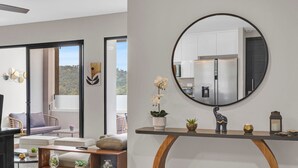 A modern living room with a sofa, coffee table, and decorative plants. A large mirror reflects the kitchen area with white cabinets and a refrigerator. - Beautiful, cozy, upscale APT next to Las Ramblas (Santa Tecla)
