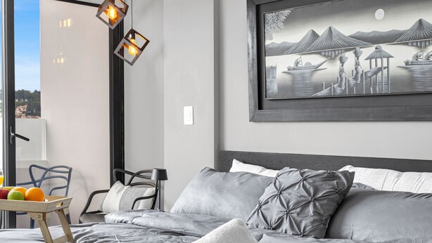 A bedroom with a bed, pillows, a tray with fruits, a chair, and a wall-mounted painting. - Beautiful, cozy, upscale APT next to Las Ramblas (Santa Tecla)