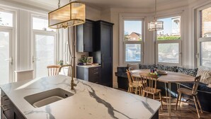 Una cocina moderna con encimera de mármol, armarios oscuros y comedor con mesa y sillas redondas.