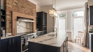 Una cocina moderna con una isla central, armarios oscuros, un muro decorativo de ladrillo y un amplio ventanal que proporciona luz natural.