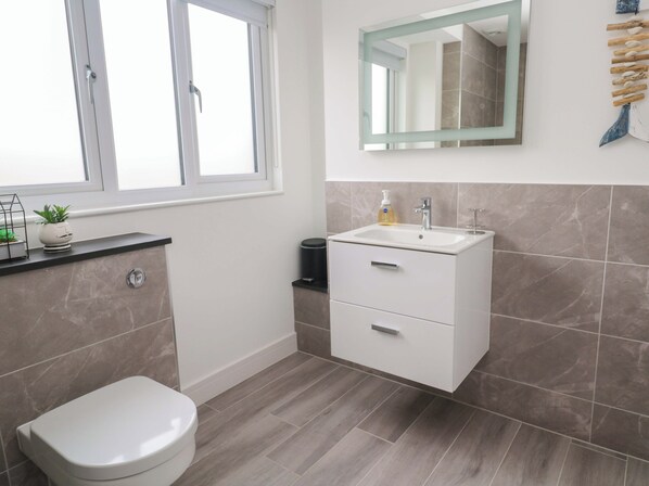 A modern bathroom with a toilet, a sink with a mirror above it, and a window. - Miramar (St Ives)