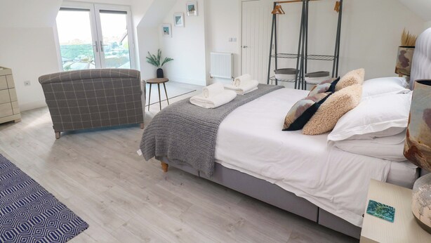 Quarto com cama, cadeira, mesinha e janela.