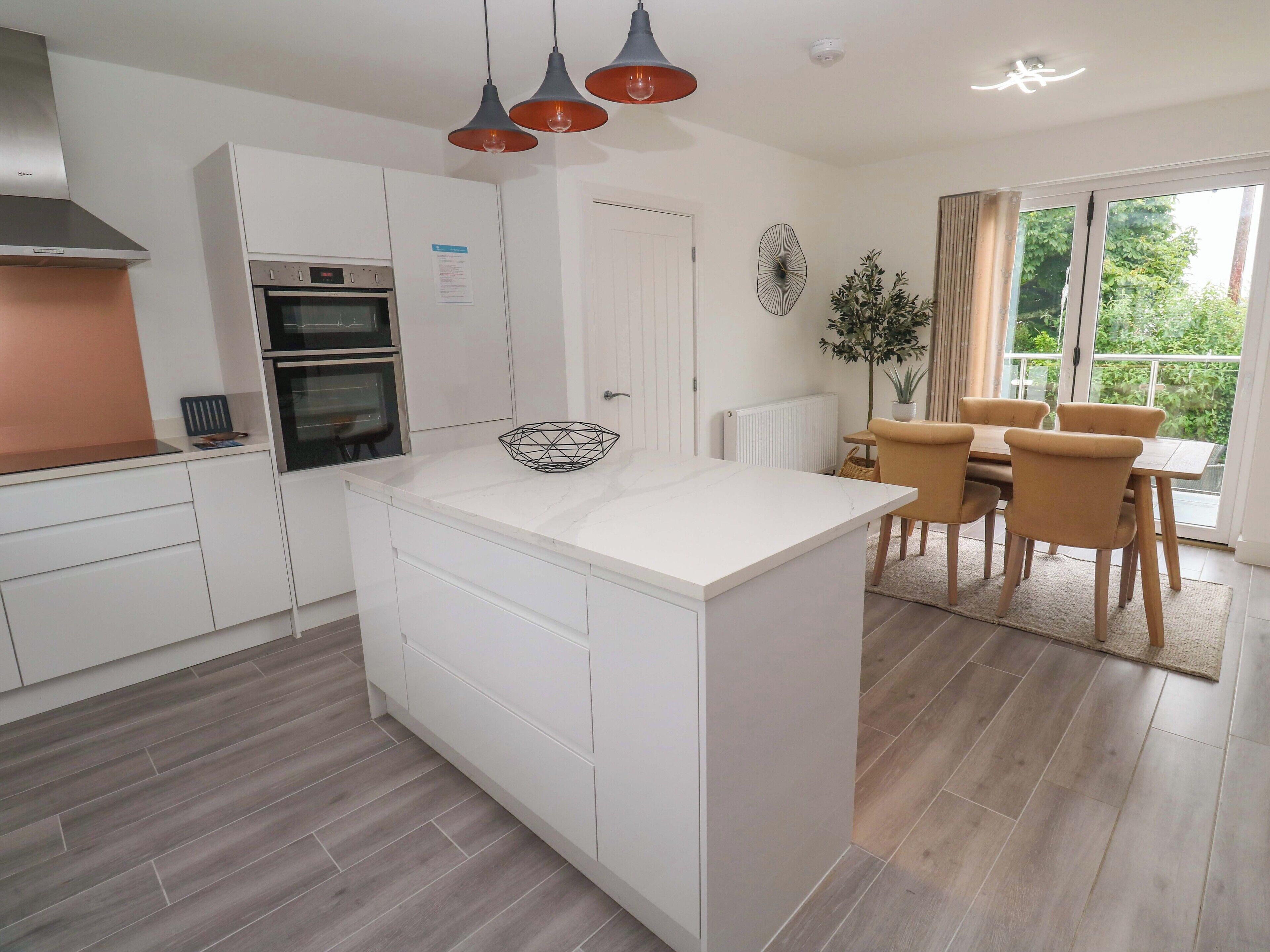 Una cocina moderna con armarios blancos, una isla central y una zona de comedor con mesa y sillas.
