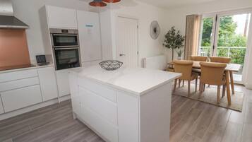 Una cocina moderna con armarios blancos, una isla central y una zona de comedor con mesa y sillas.