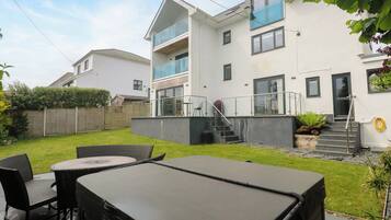 A modern two-story house with a balcony, a patio with outdoor furniture, and a well-maintained garden.