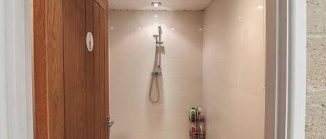 A shower stall with a wooden door, tiled walls, and a showerhead.