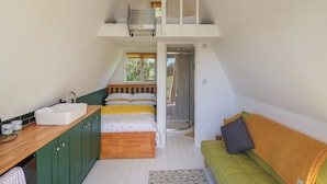 A compact room with a loft bed, a kitchen area, and a green sofa. - A-frame (Woodbridge)