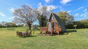 A wooden cabin with a triangular roof, a deck, and a table with chairs in front. - A-frame (Woodbridge)