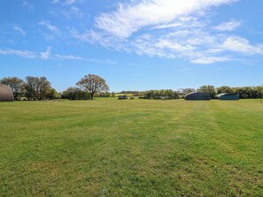 A grassy field with a large tree, barns, and a clear sky. - Robin (Woodbridge)