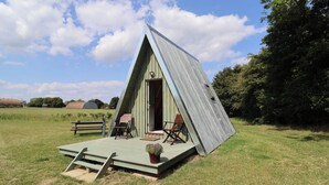 A triangular A-frame structure with a porch and two chairs. - Robin (Woodbridge)