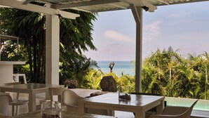 An outdoor dining area with tables and chairs, overlooking a tropical landscape and the ocean.