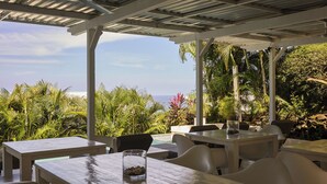 An outdoor dining area with tables and chairs, overlooking a view of the ocean and lush greenery.