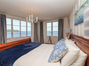 A bedroom with a large bed, a chandelier, and a view of the sea through large windows. - Marina (Torpoint)
