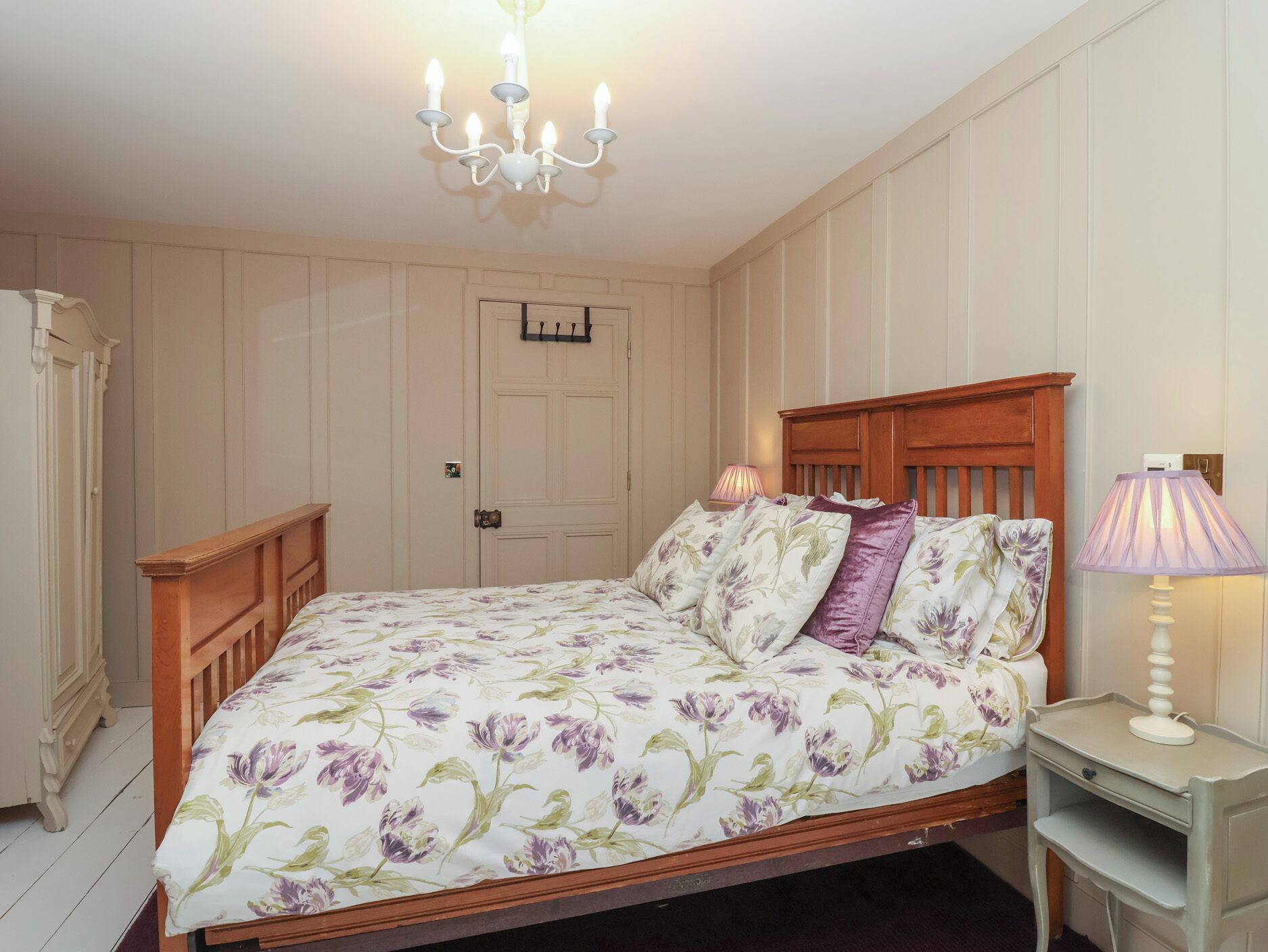 A bedroom with a floral bedspread, a wooden headboard, a nightstand with a lamp, and a wardrobe.