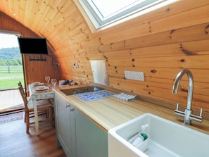 A compact kitchen with wooden walls, a sink, and a window overlooking a green landscape. - Bwthyn Bach Brefi (Tregaron)
