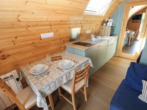 A compact kitchen with a dining area, wooden walls, a skylight, and a small table set for two. - Bwthyn Bach Brefi (Tregaron)