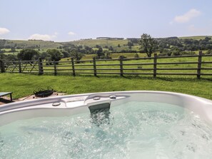 Un bain à remous avec vue sur des collines verdoyantes et entouré d’une clôture en bois.