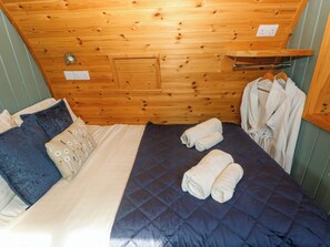 Una habitación con paneles de madera, una cama, almohadas, una colcha acolchada y toallas enrolladas.
