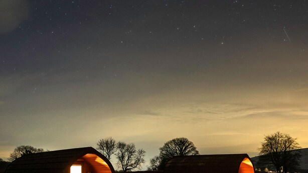 Two barns with open doors, one with a bench and a table visible inside, set against a starry night sky. - Bwthyn Bach Brefi (Tregaron)