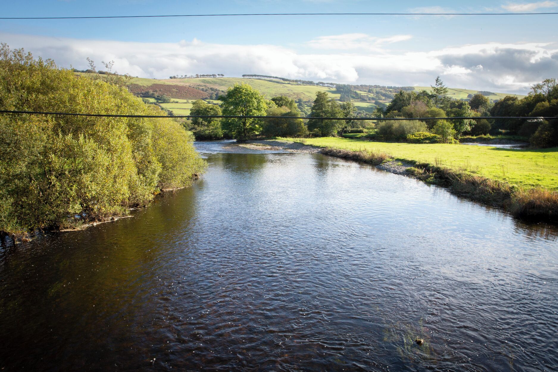 A river flowing through a rural landscape with grassy banks and trees.