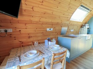 A wooden cabin with a dining area set for two, a kitchenette, and a TV mounted on the wall. - Bwthyn Bach Brefi (Tregaron)