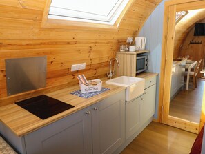 A compact kitchen with wooden walls, a built-in microwave, a sink, and a small window above the countertop. - Ty Twt Teifi (Tregaron)