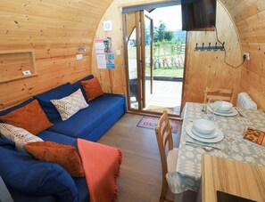 A cozy wooden interior with a sofa, a dining table set with plates and glasses, and a view of the outdoors. - Ty Twt Teifi (Tregaron)