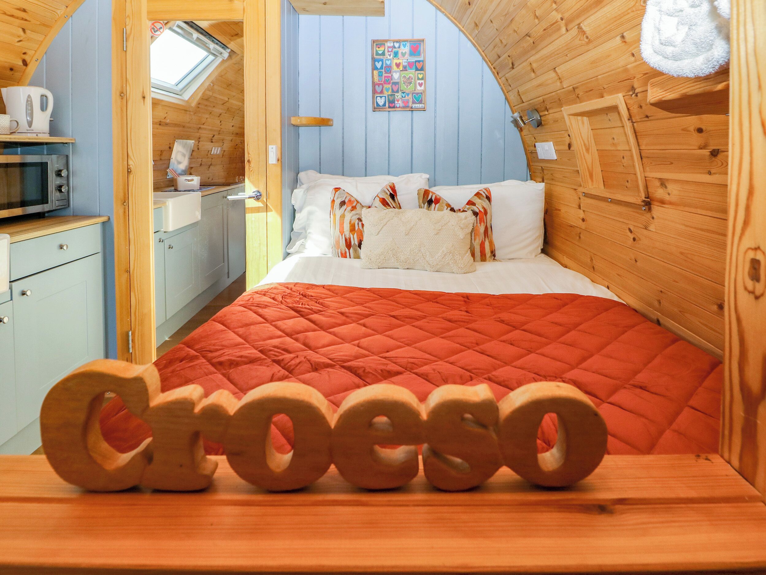 A cozy room with a bed, a wooden wall, a window, and a kitchenette.