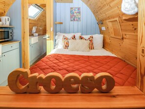 A cozy room with a bed, a wooden wall, a window, and a kitchenette. - Ty Twt Teifi (Tregaron)