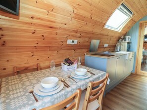 A wooden interior with a dining table set for two, a kitchen area, and a skylight. - Ty Twt Teifi (Tregaron)