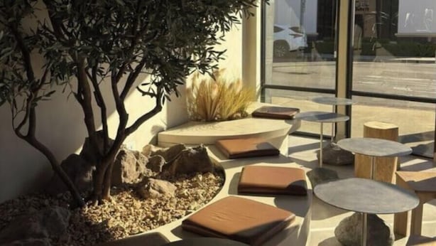 Zona d'estar exterior amb taules rodones i bancs amb coixins, envoltada de roques i plantes.