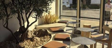 Un espace extérieur aménagé avec des tables rondes et des bancs rembourrés, entouré de rochers et de plantes.