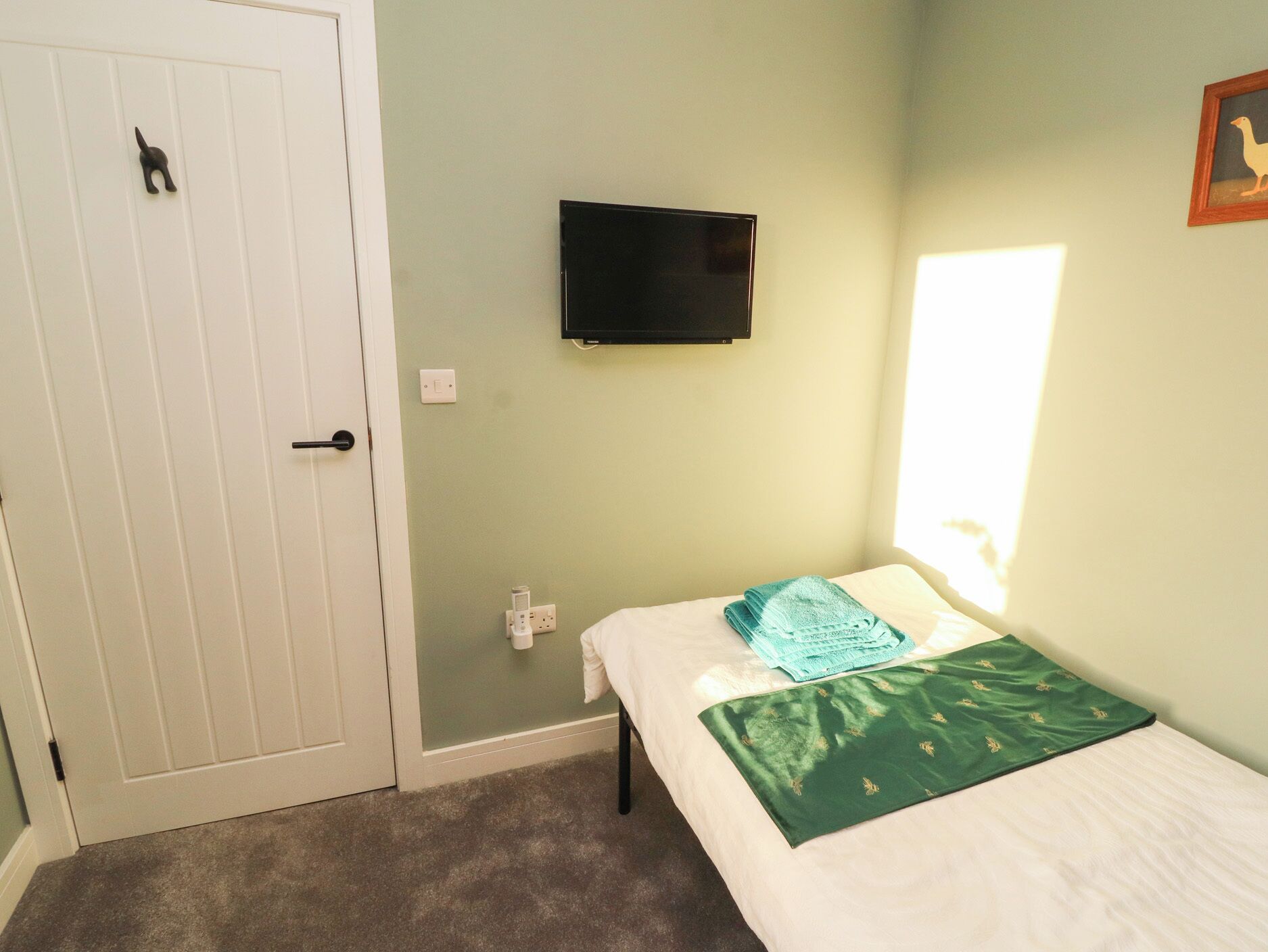 Un dormitorio con cama, televisor montado en la pared, una puerta y una ventana.