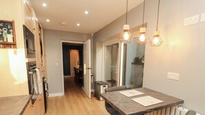 A modern kitchen with wooden cabinets, a dining table with two chairs, and pendant lights. - 10 Keekle Terrace (Cleator Moor)
