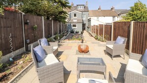 A patio with wicker furniture and a fire pit, surrounded by a wooden fence and a garden. - 10 Keekle Terrace (Cleator Moor)